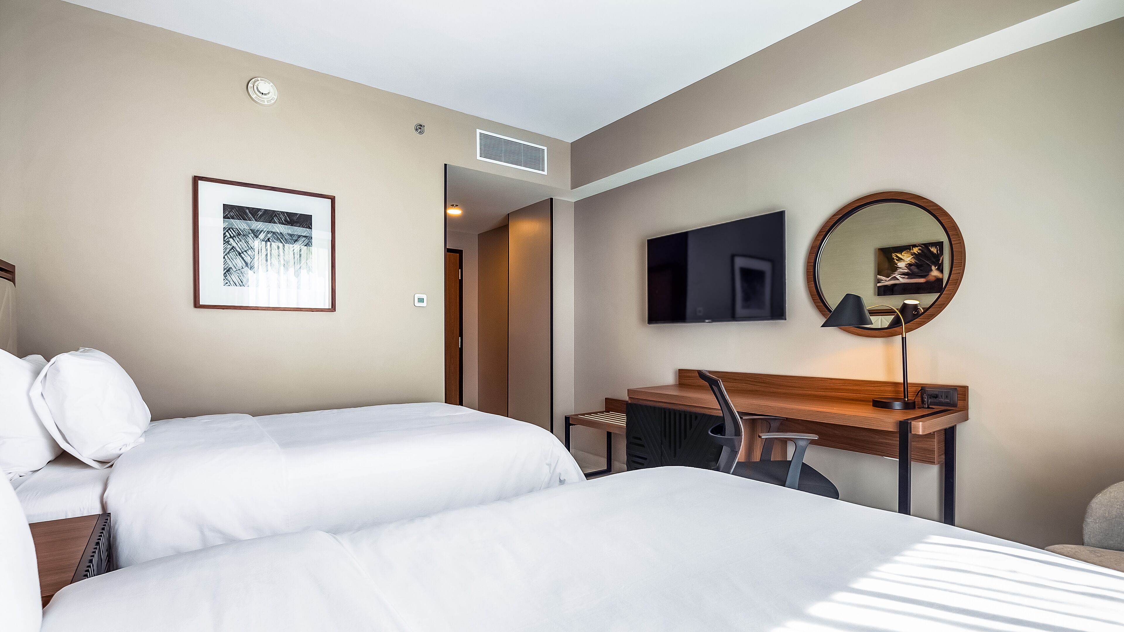 A hotel room with a bed, a desk, a chair, a TV, a mirror, and a framed picture on the wall.