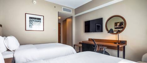 A hotel room with a bed, a desk, a chair, a TV, a mirror, and a framed picture on the wall.