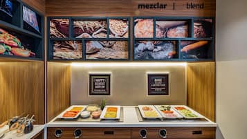 Un bufé de desayuno con diversas opciones de alimentos y una pared que exhibe imágenes de cereales y pan.