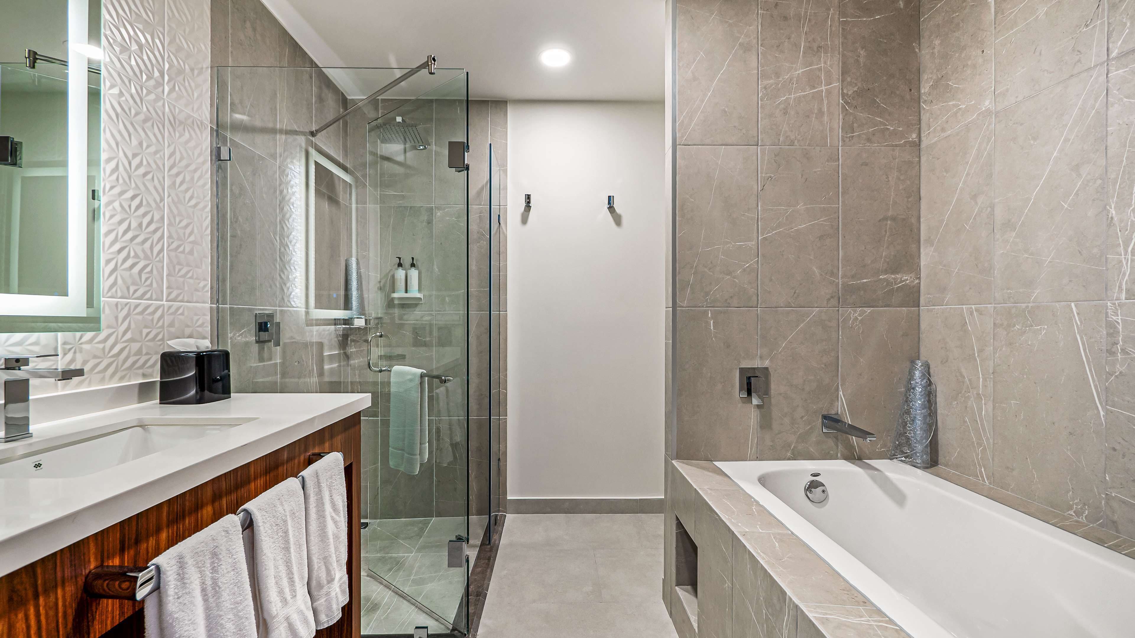 Un baño moderno con cabina de ducha de vidrio, una bañera independiente y un tocador con espejo y dos lavamanos.