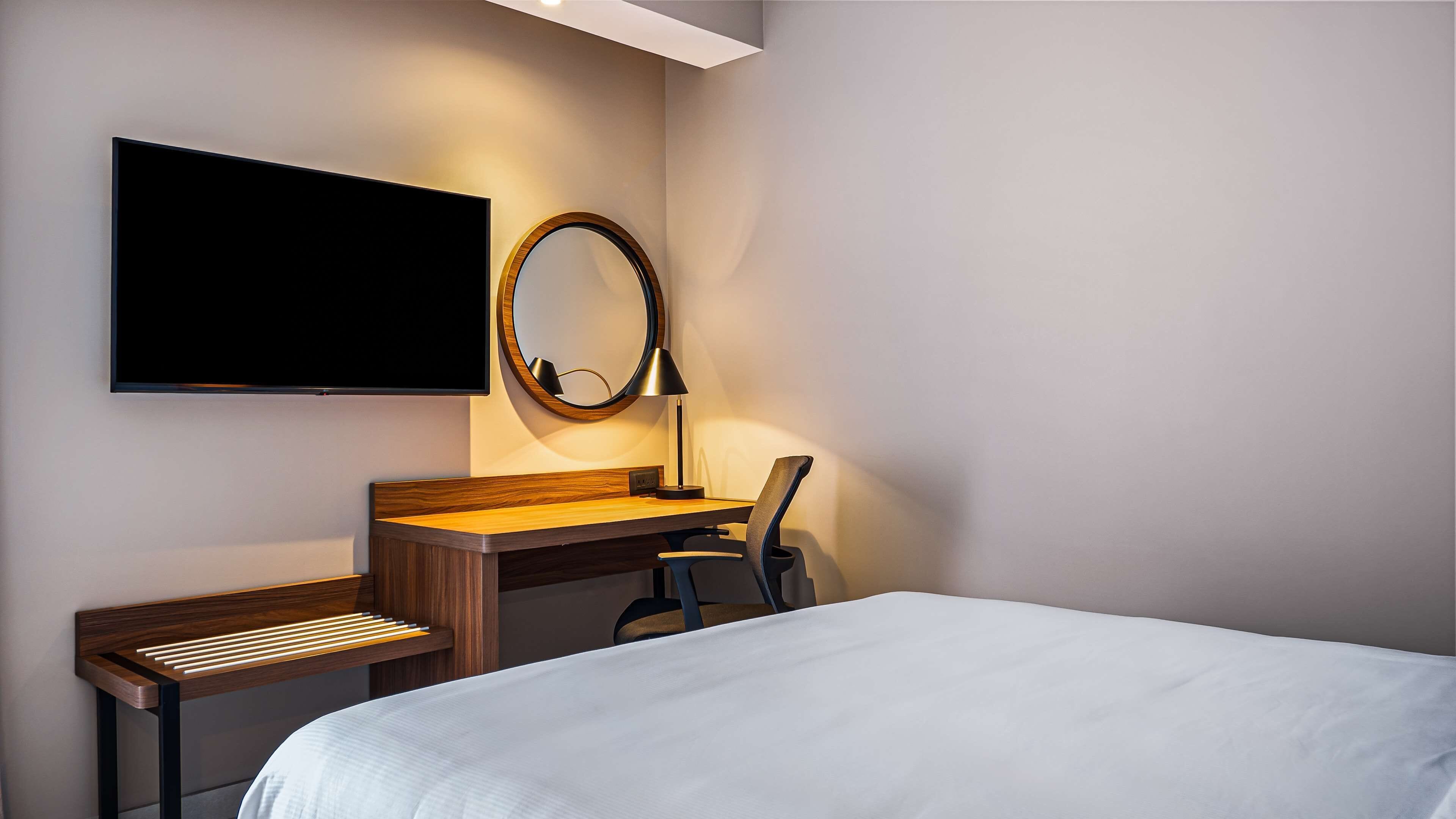 A hotel room with a bed, a desk with a chair, a TV, and a mirror.