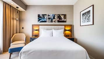 Habitación de hotel con una cama grande, una silla y una mesita de noche con una lámpara. Encima de la cama hay tres cuadros enmarcados en la pared.