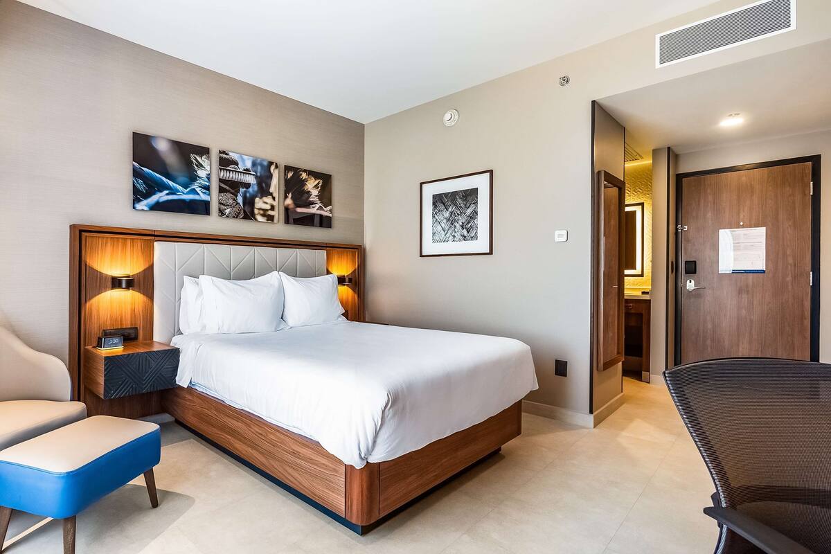 A modern hotel room with a large bed, a desk, a chair, and a small table.