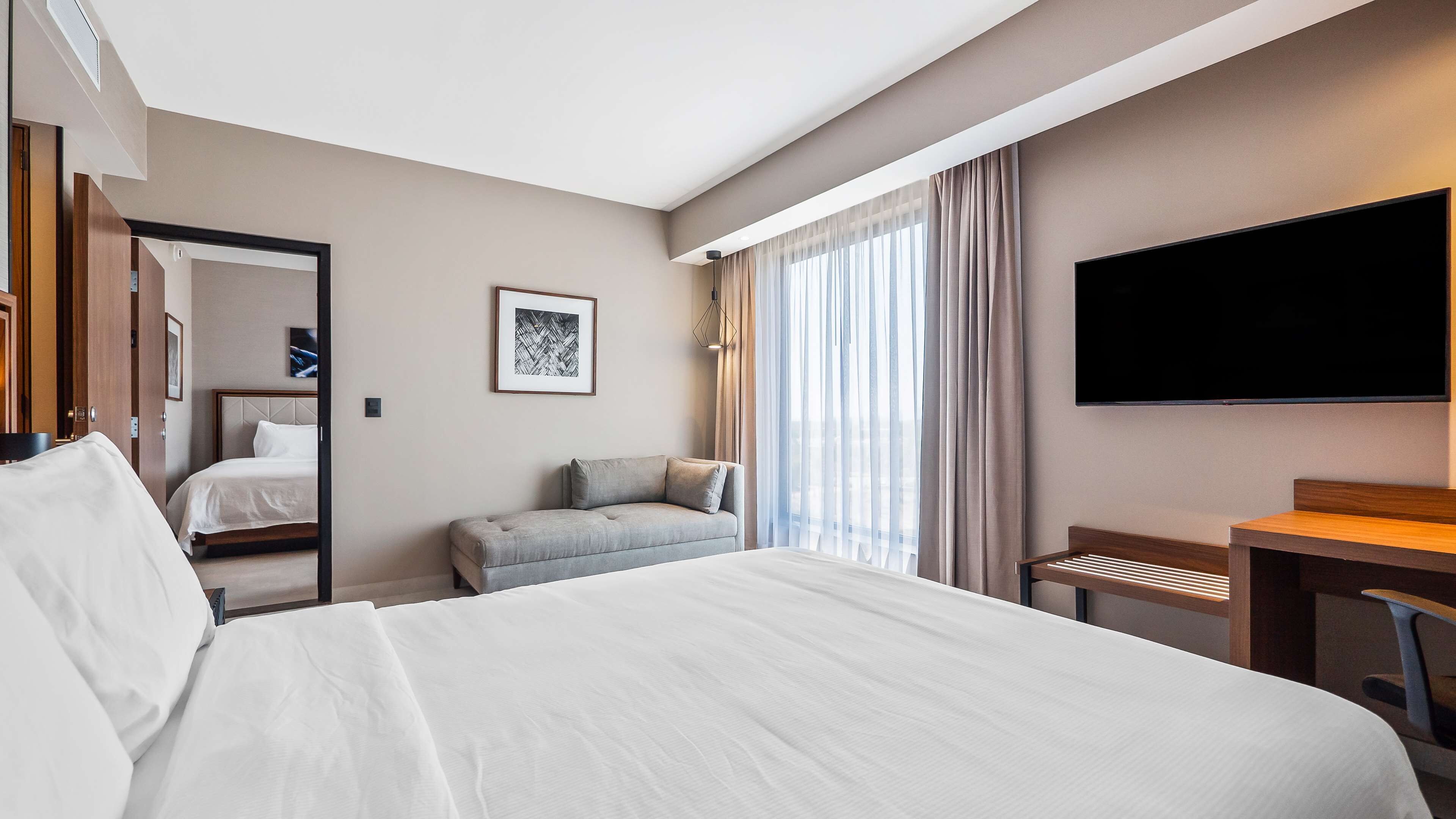 Habitació d'hotel amb un llit gran, una taula de treball, una cadira, una televisió i una finestra amb cortines.