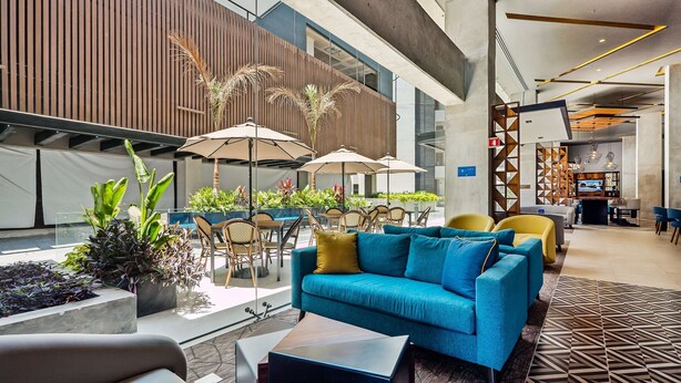 Un vestíbulo moderno con un sofá azul, sillas amarillas y zona de estar exterior con sombrillas.
