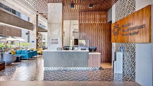 Un moderno vestíbulo de hotel con mostrador de recepción, área de descanso y una pared decorativa con patrones geométricos.