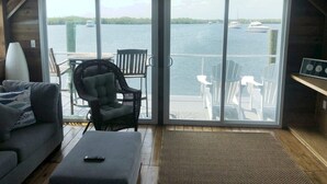 Una sala de estar con un gran ventanal corredera que da a un balcón con vista al agua y barcos.