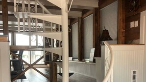 Una escalera de caracol con barandillas blancas y escalones negros, que conduce a una terraza de madera con mobiliario exterior.