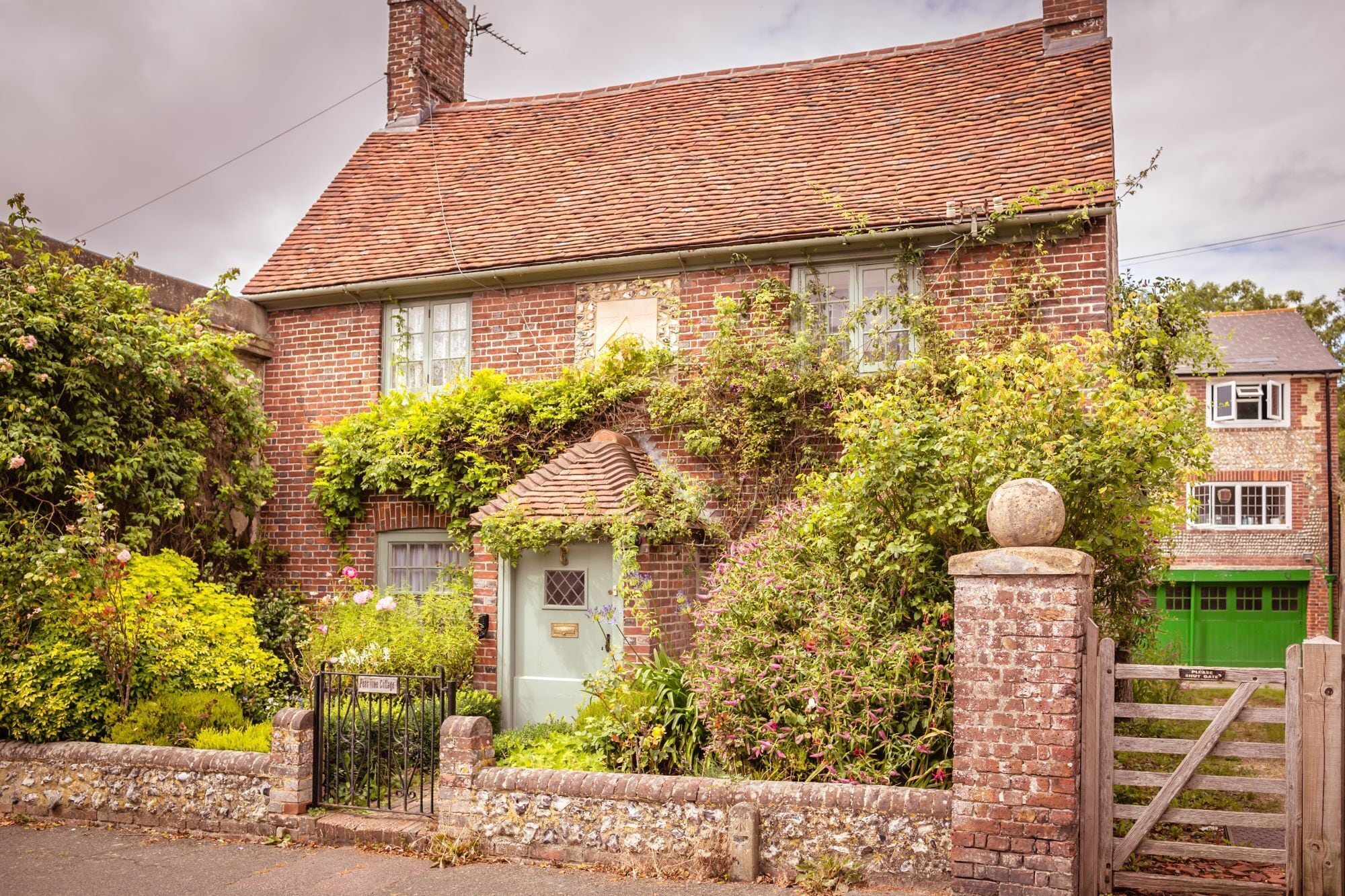 Une maison traditionnelle en briques, avec un toit en tuiles, des murs couverts de lierre et un portail à l’avant.