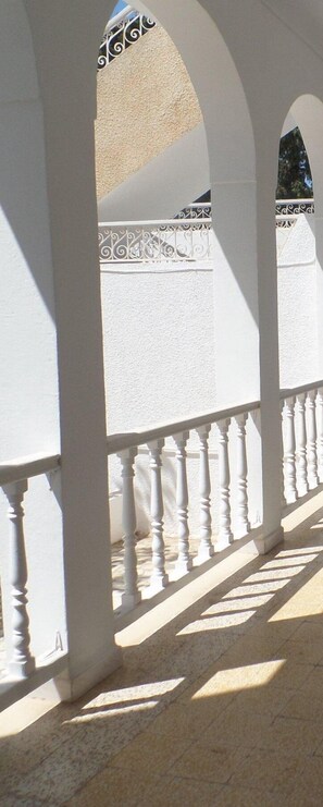 Een overdekt buitengebied met witte zuilen en een balustrade.