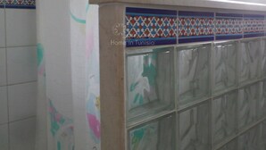 A bathroom with a tiled wall, a window with curtains, and a tiled shower area. - Vacation home in hammamet (Hammamet)