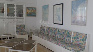 A living room with a white sofa, two glass-top coffee tables, a white cabinet with glass doors, and three framed artworks on the wall. - Vacation home in hammamet (Hammamet)