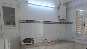 A compact kitchen with white cabinets, a microwave, a sink, and a small dining area with a chair. - Vacation home in hammamet (Hammamet)