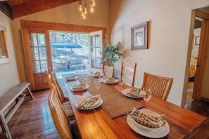 A dining area with a wooden table set for four, surrounded by wicker chairs, with a view of an outdoor patio. - Granite Getaway: Spacious and Beautiful, Hot Tub, Dog Friendly, Backs Forestland by Tahoe Time VR (Carnelian Bay)
