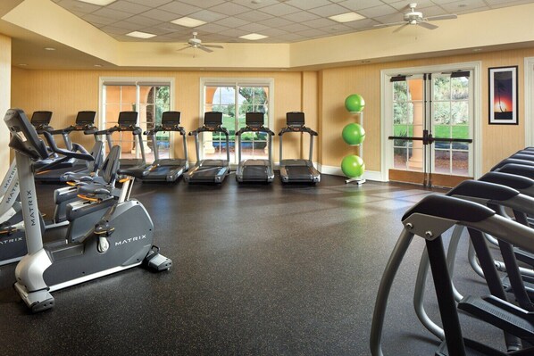 Une salle de sport équipée de tapis de course, de vélos elliptiques et de ballons d’exercice.