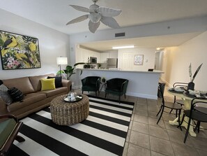 A living room with a brown sofa, green chairs, a striped rug, and a dining area with a table and chairs.