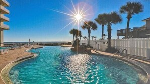 Una piscina con agua cristalina, rodeada de palmeras y una valla blanca.