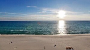 Una playa con cielo despejado y el sol reflejándose en el agua.