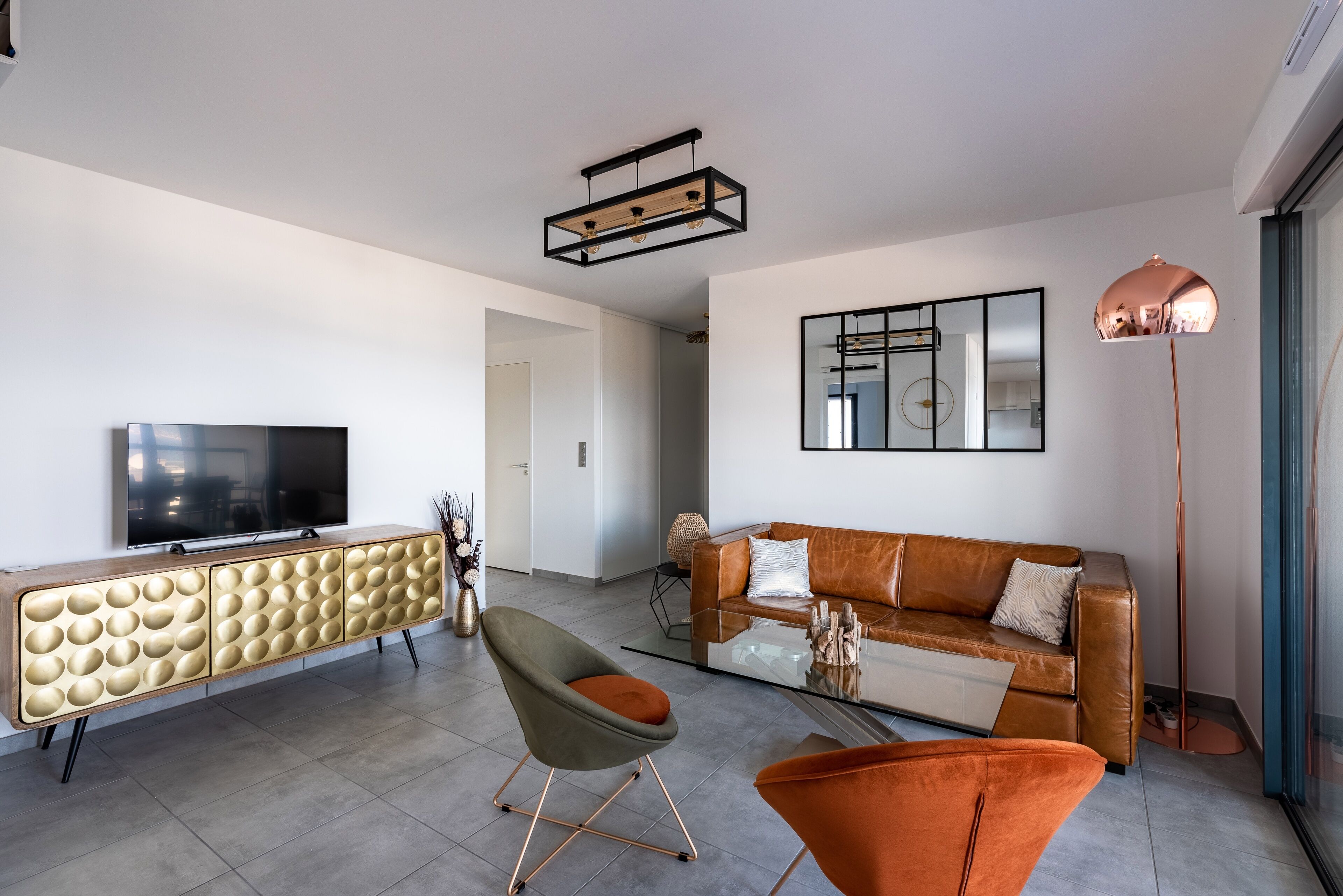 A modern living room with a flat-screen TV, a leather sofa, a glass coffee table, and a unique wooden cabinet.
