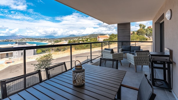 Ein Balkon mit Blick auf Strand und Berge, ausgestattet mit Korbstühlen und einem Tisch.