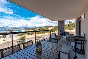 Un balcon avec vue sur une plage et des montagnes, aménagé avec des fauteuils et une table en osier.