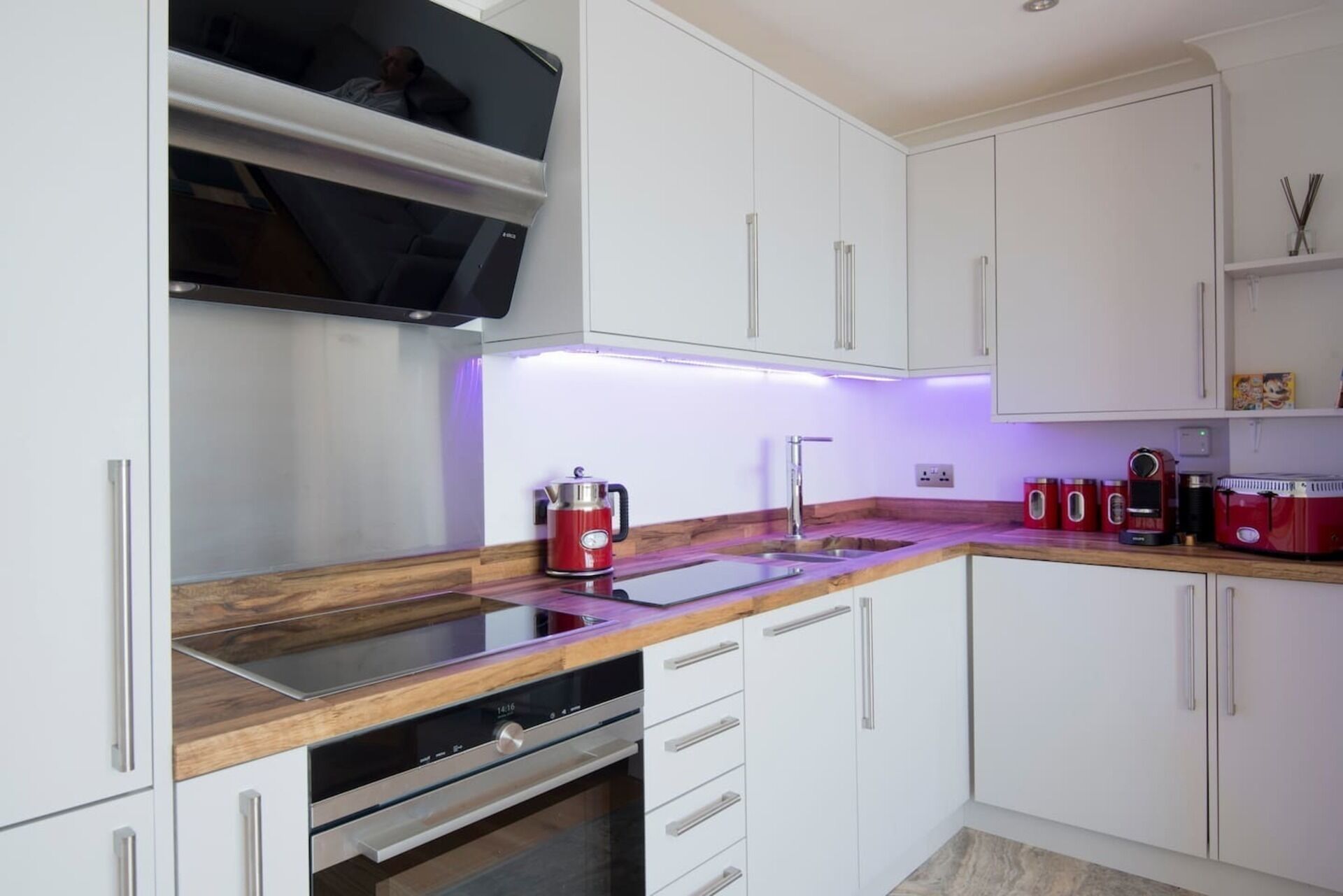 A modern kitchen with white cabinets, a wooden countertop, a built-in oven, and a coffee machine.