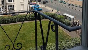 Uitzicht op de kust vanaf een balkon met een hekwerk, met daaronder een weg met geparkeerde auto's en een strand in de verte.
