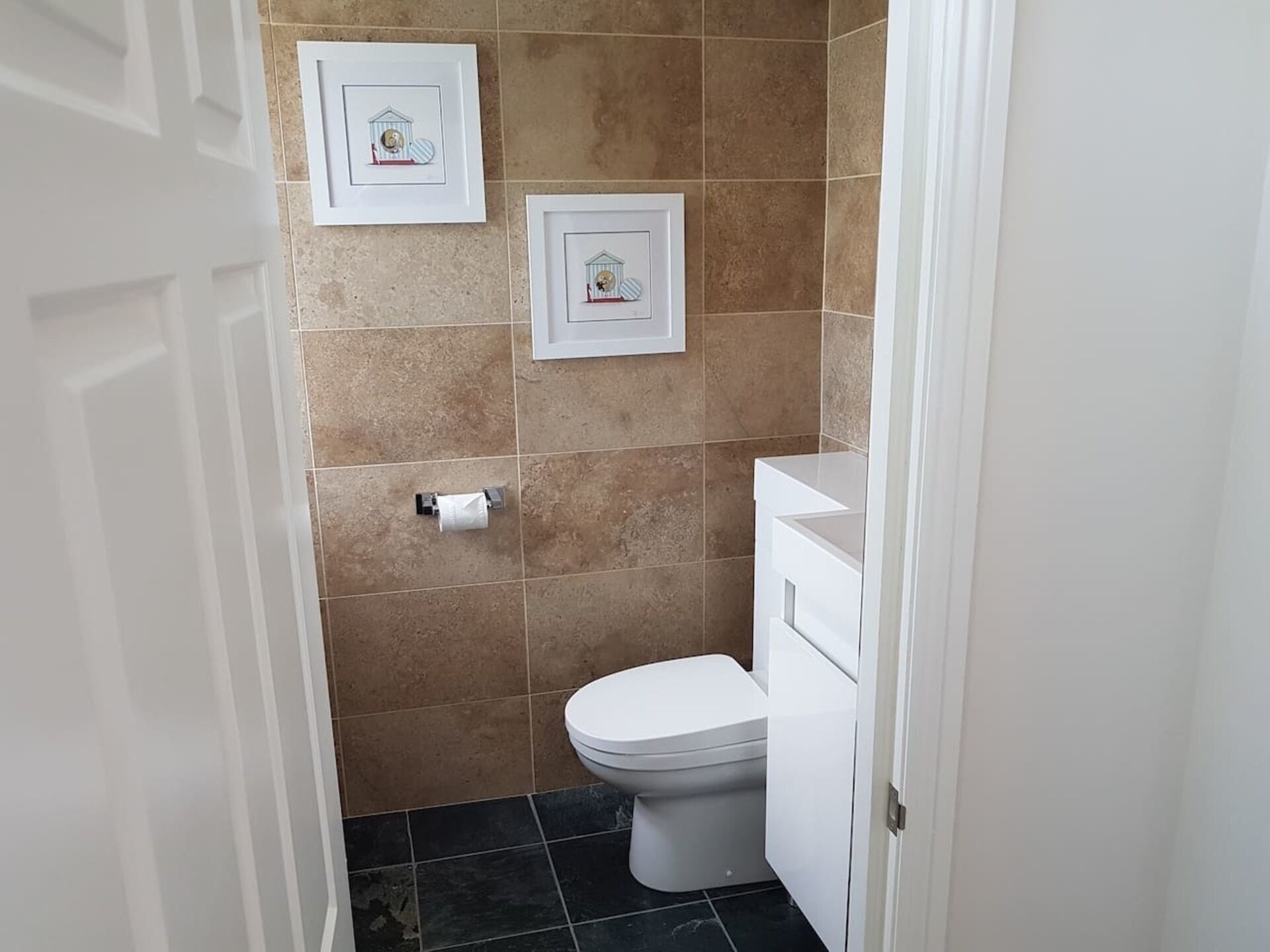 A small bathroom with a toilet, a sink, and two framed pictures on the wall.