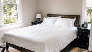 Ein Schlafzimmer mit einem großen Bett, zwei Nachttischen und einem Fenster mit Blick auf Grünflächen.