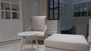 Un saló modern amb un butaquetó beix, una taula rodona blanca i un pouf a joc.