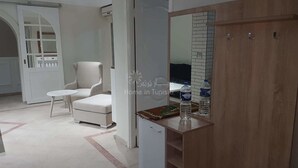 Habitació amb una poltrona blanca, una taula rodona petita, un armari de fusta i una façana de rajola.