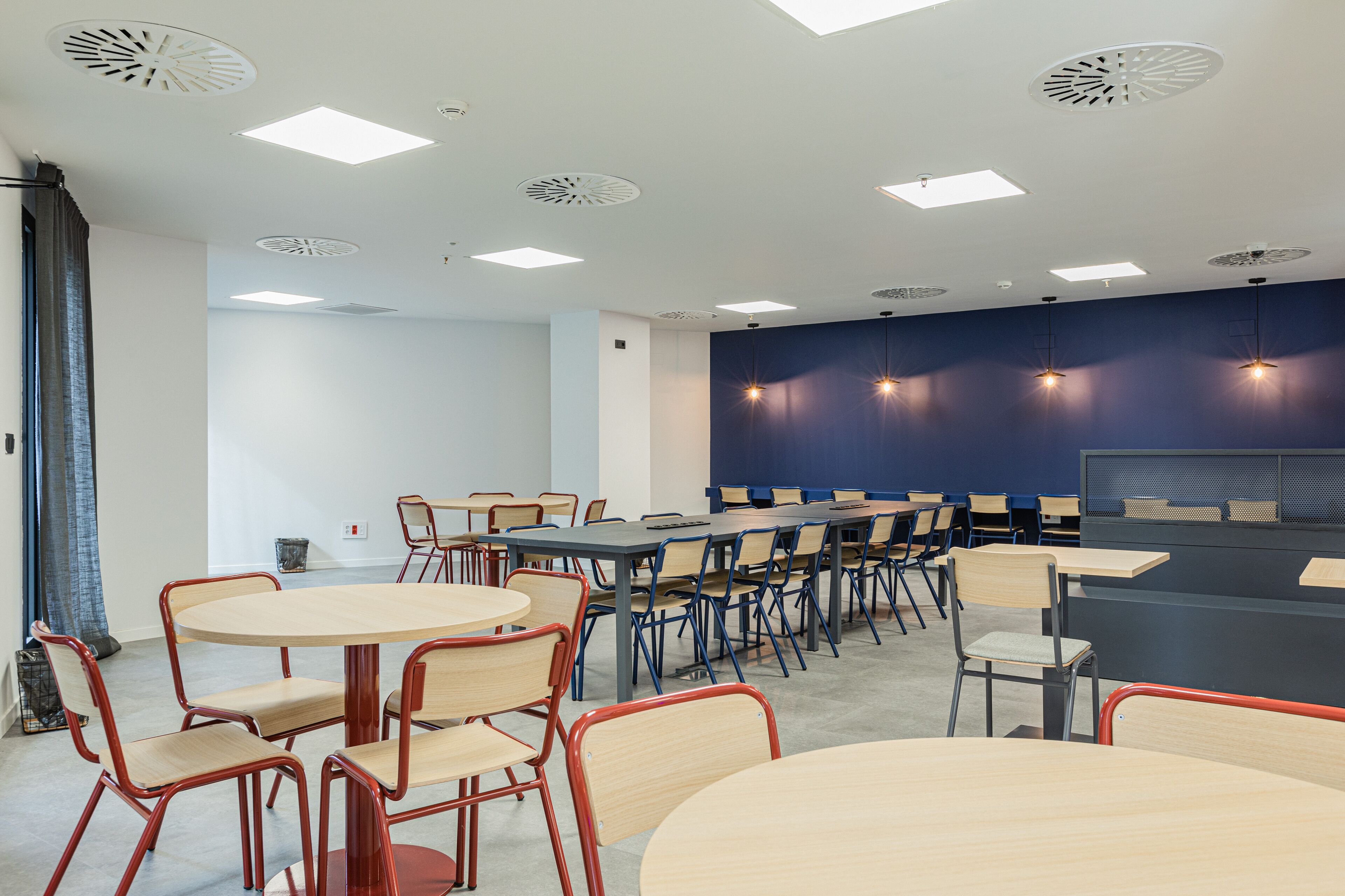 A conference room with round tables and chairs, a dark blue accent wall, and recessed ceiling lights.