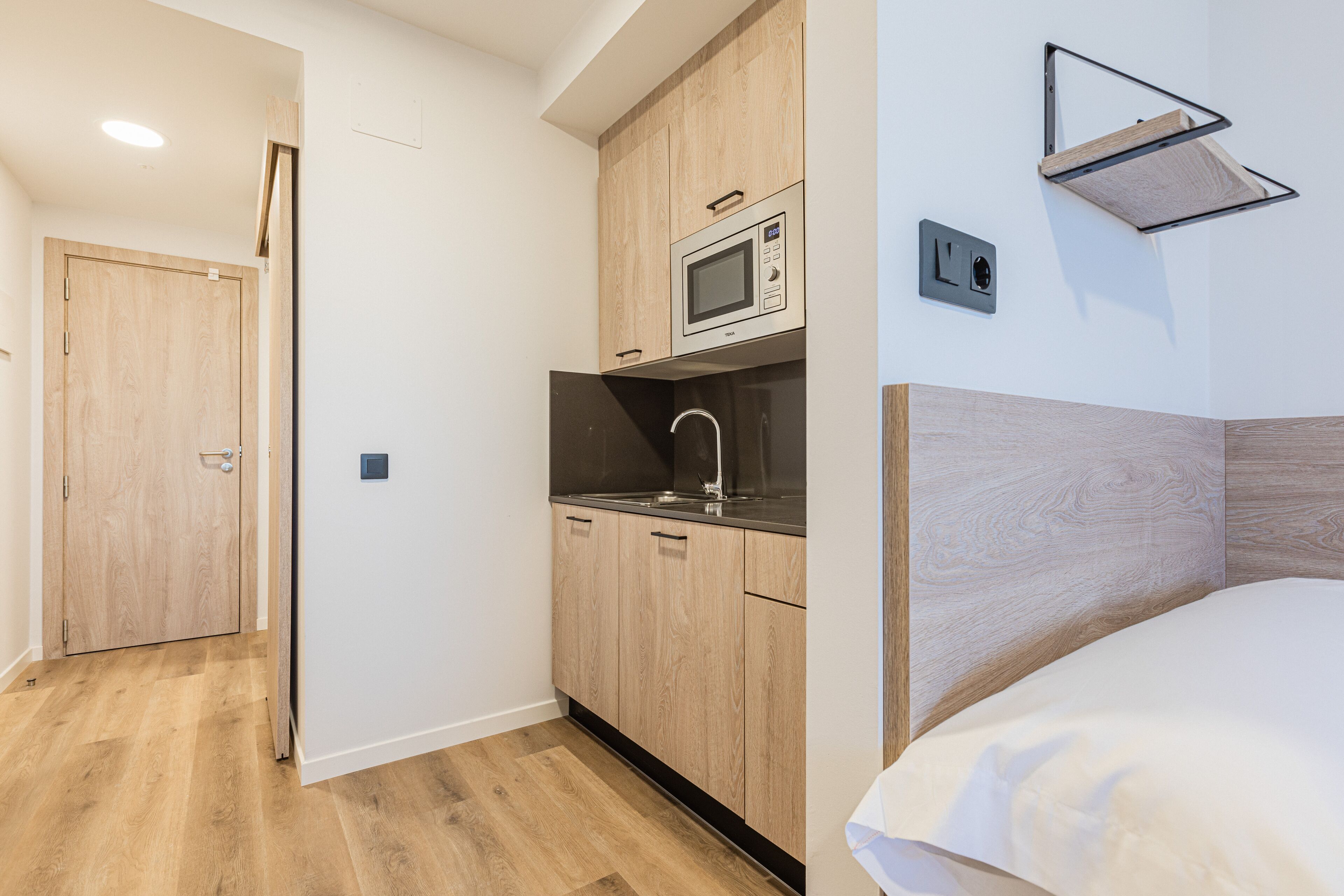 Une cuisine de taille réduite, équipée d’un four à micro-ondes, d’un évier et de meubles de rangement en bois.