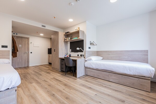 Une chambre d’hôtel moderne avec un plancher en bois, un lit, un bureau avec une chaise et une armoire.