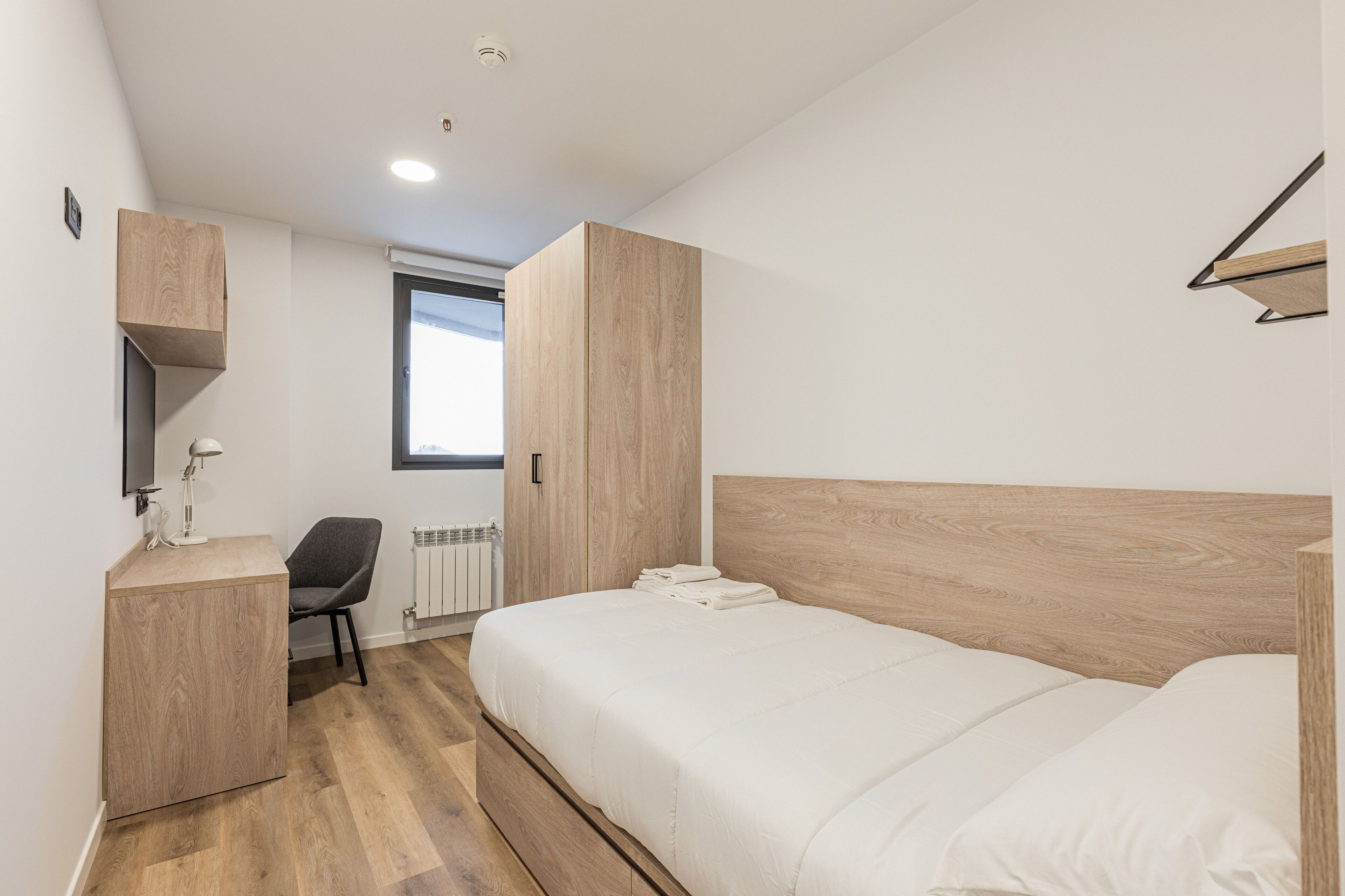Un dormitorio moderno con cabecera de madera, un escritorio con silla y una ventana que proporciona luz natural.