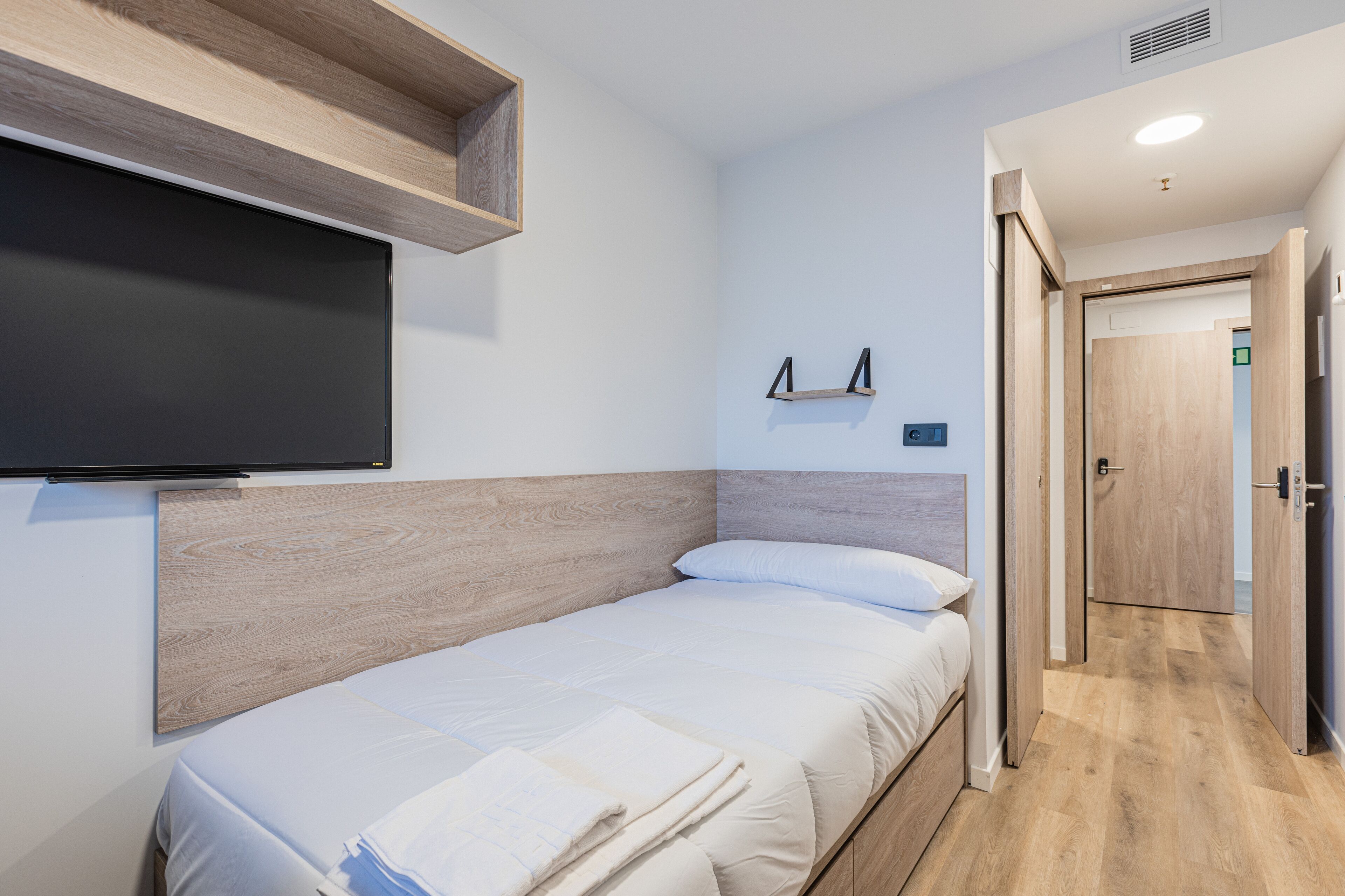 A neatly arranged bedroom with a bed, a mounted TV, and a wooden headboard.