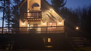 Una baita di legno a due piani con un balcone, un'ampia finestra e una veranda.