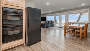 Een moderne keuken met inbouwapparatuur, een eethoek met een grote tafel en stoelen, en een uitzicht door de ramen.
