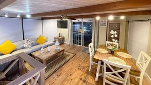 A cozy living area with a sofa, coffee table, and dining table. There is a TV mounted on the wall and a window with curtains. - Aqua Lodge Houseboat "Captain's Quarters" (Tavernier)