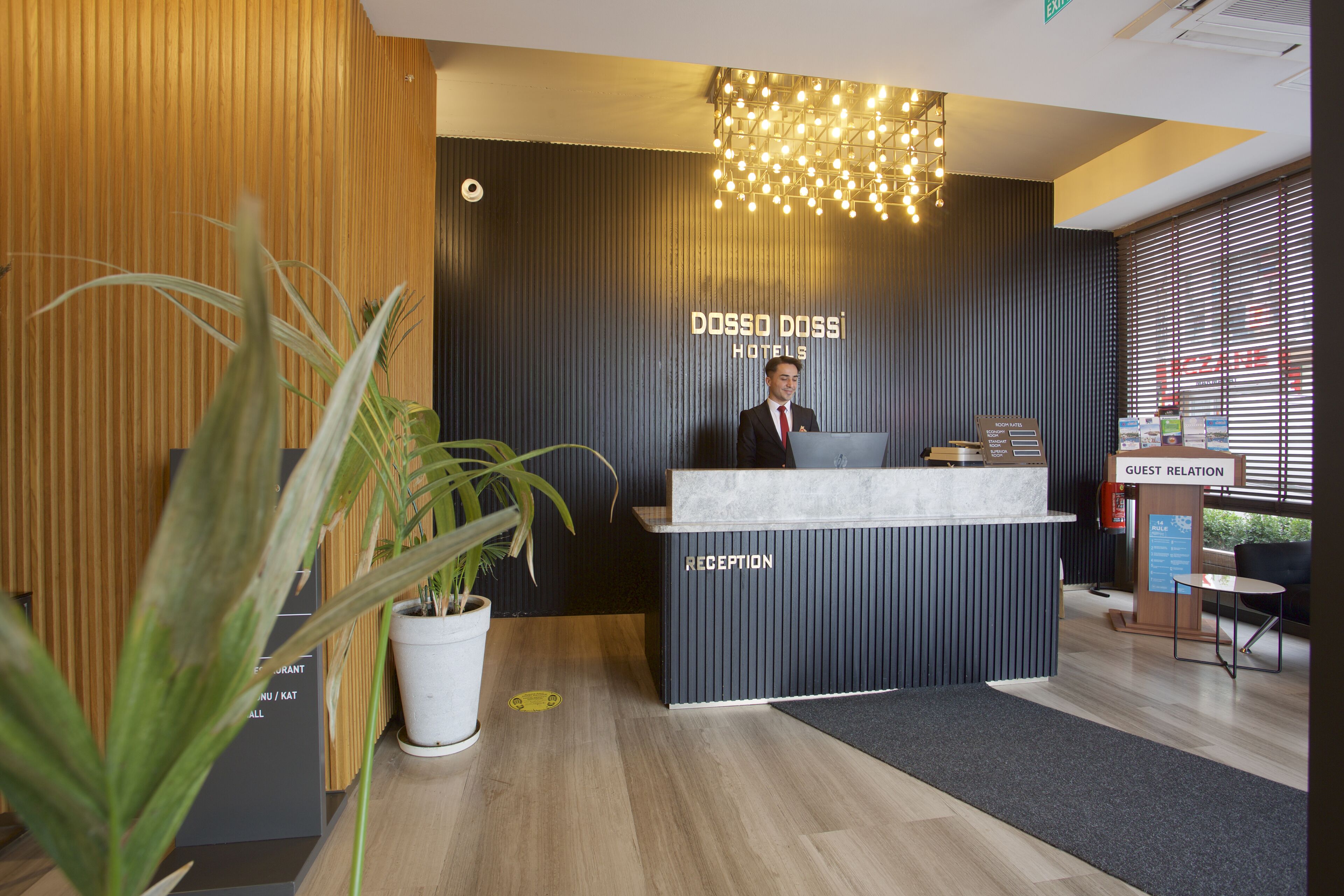 A reception desk with a modern design, a sign for 'DOSSO DOSSI HOTELS', and a 'GUEST RELATION' sign.