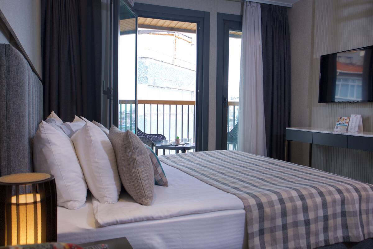 A hotel room with a bed, a desk, a TV, and a balcony with curtains.