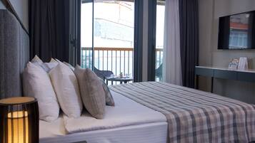 A hotel room with a bed, a desk, a TV, and a balcony with curtains.