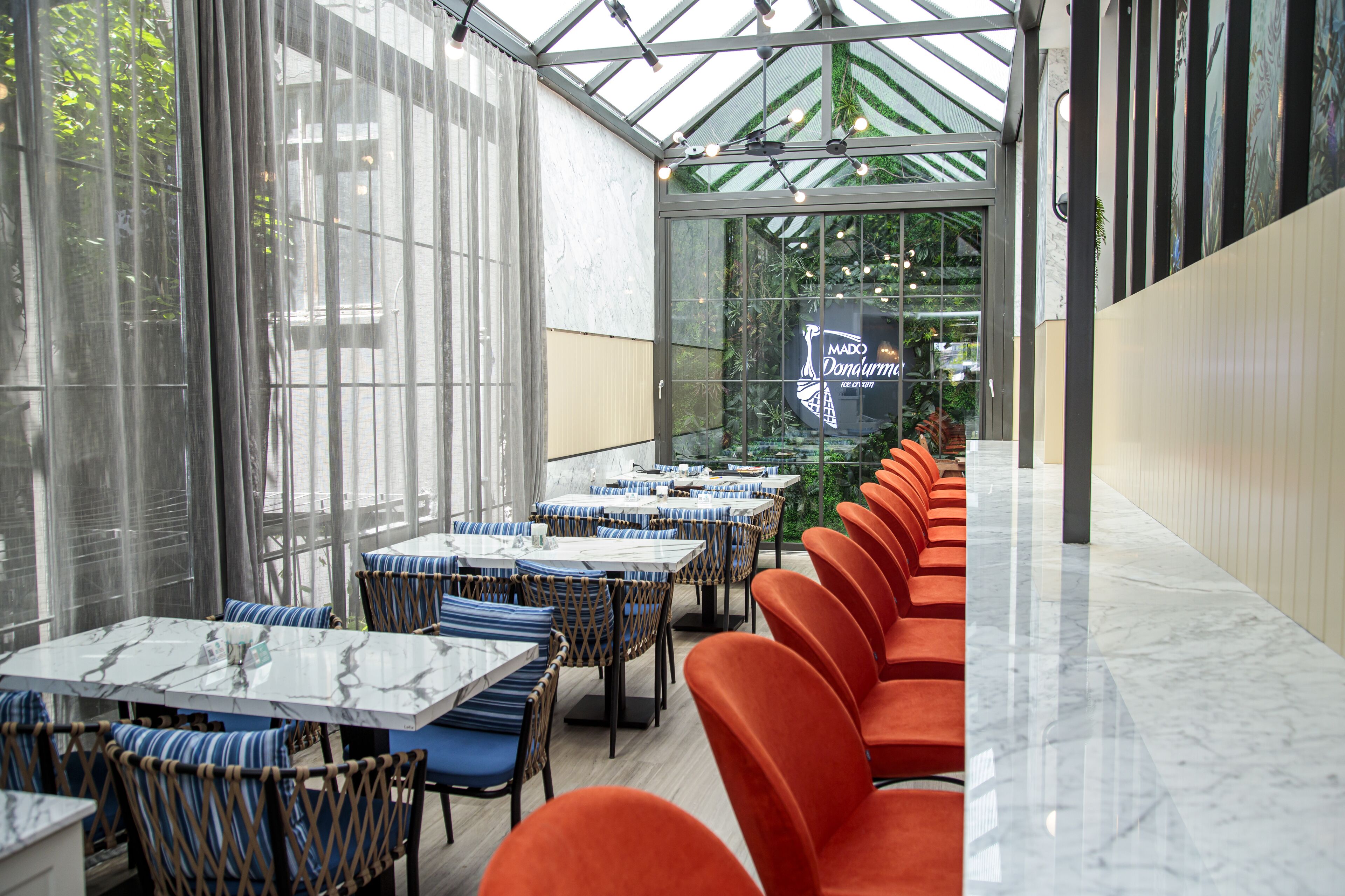 A restaurant with a long counter, blue and orange chairs, and a glass wall with a view of greenery.