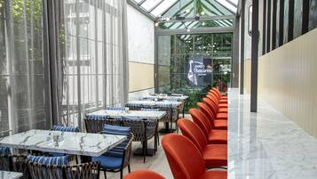 A restaurant with a long counter, blue and orange chairs, and a glass wall with a view of greenery.