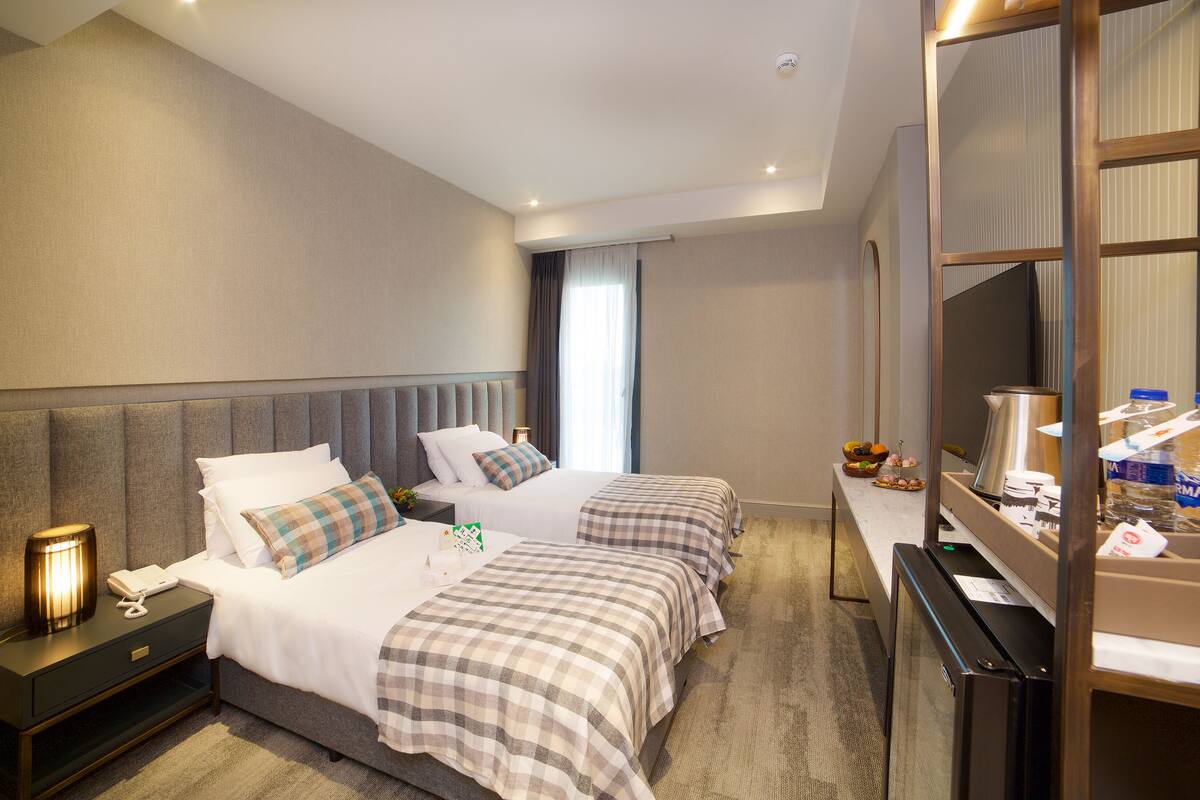 A hotel room with two beds, a desk, a mirror, and a television.