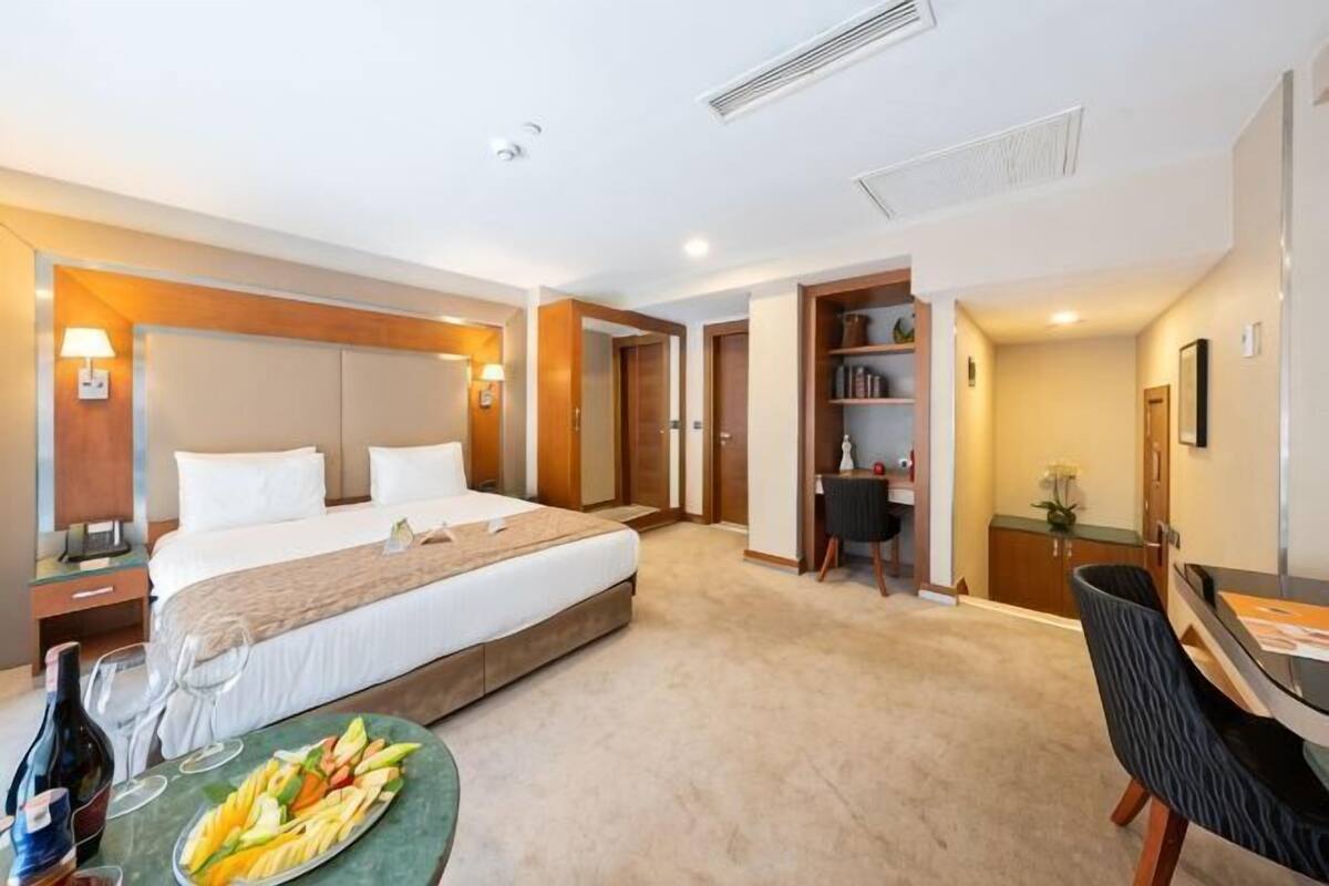 A hotel room with a bed, bedside table, a dining area with a table and chairs, a bookshelf, and a desk.