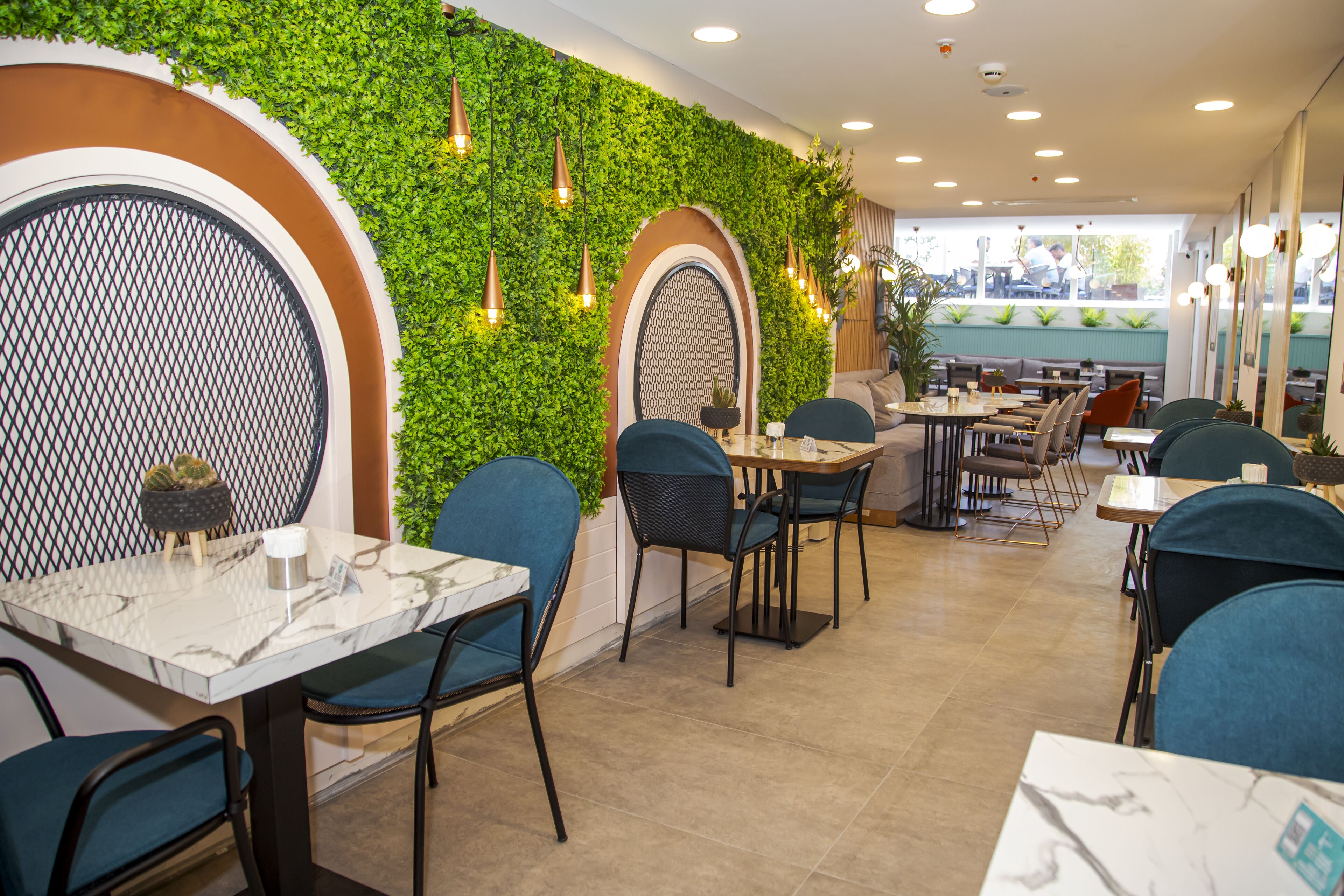 A restaurant with a green wall, marble tables, and blue chairs.