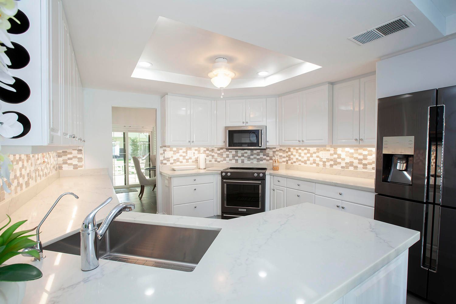 A modern kitchen with white cabinetry, a central island, a built-in oven, and a stainless steel refrigerator.