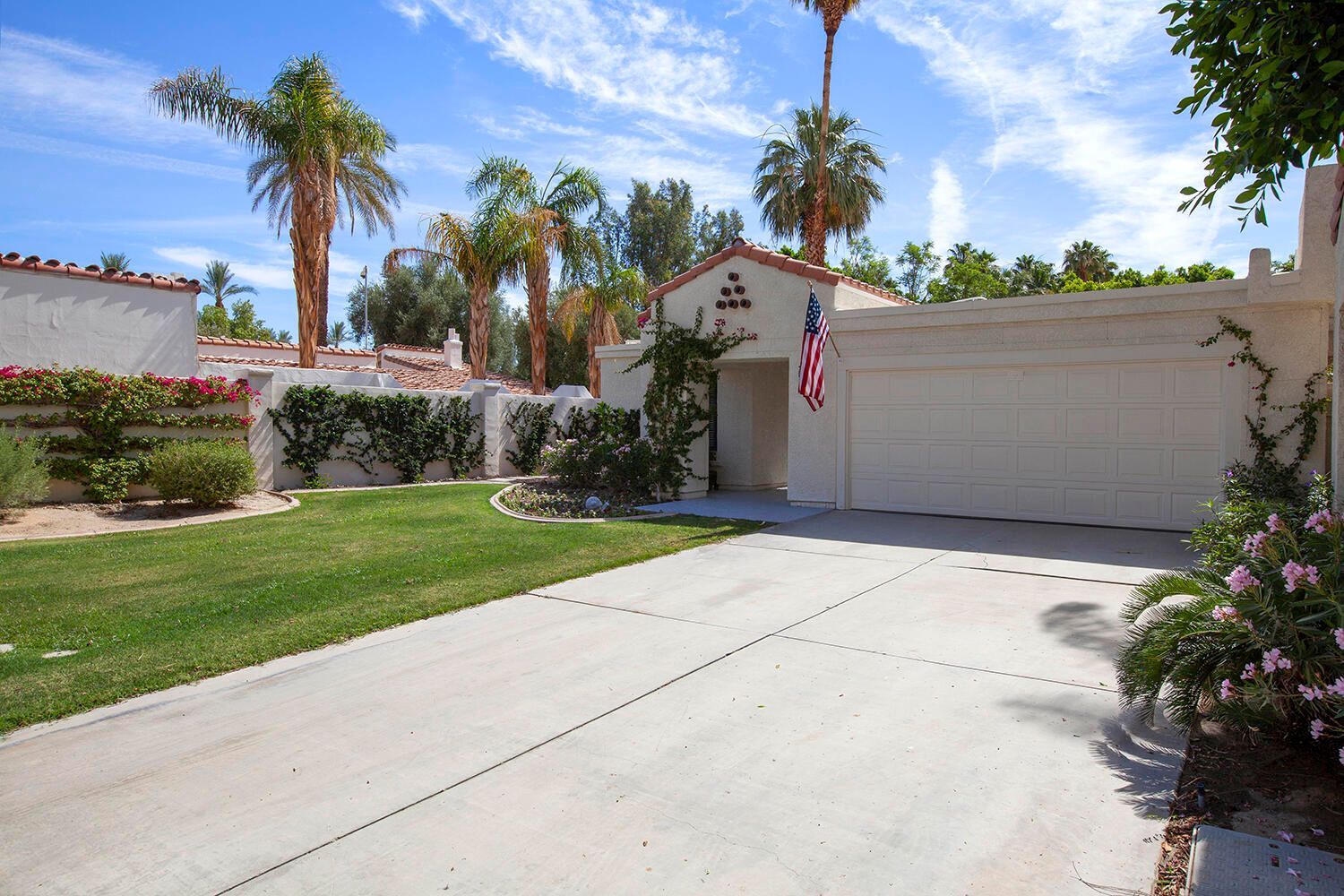 A residential driveway with a white garage, a well-maintained lawn, and a row of palm trees in the background.