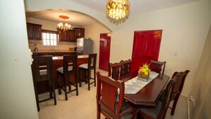 Un comedor con una mesa y sillas de madera, una araña y una cocina al fondo.